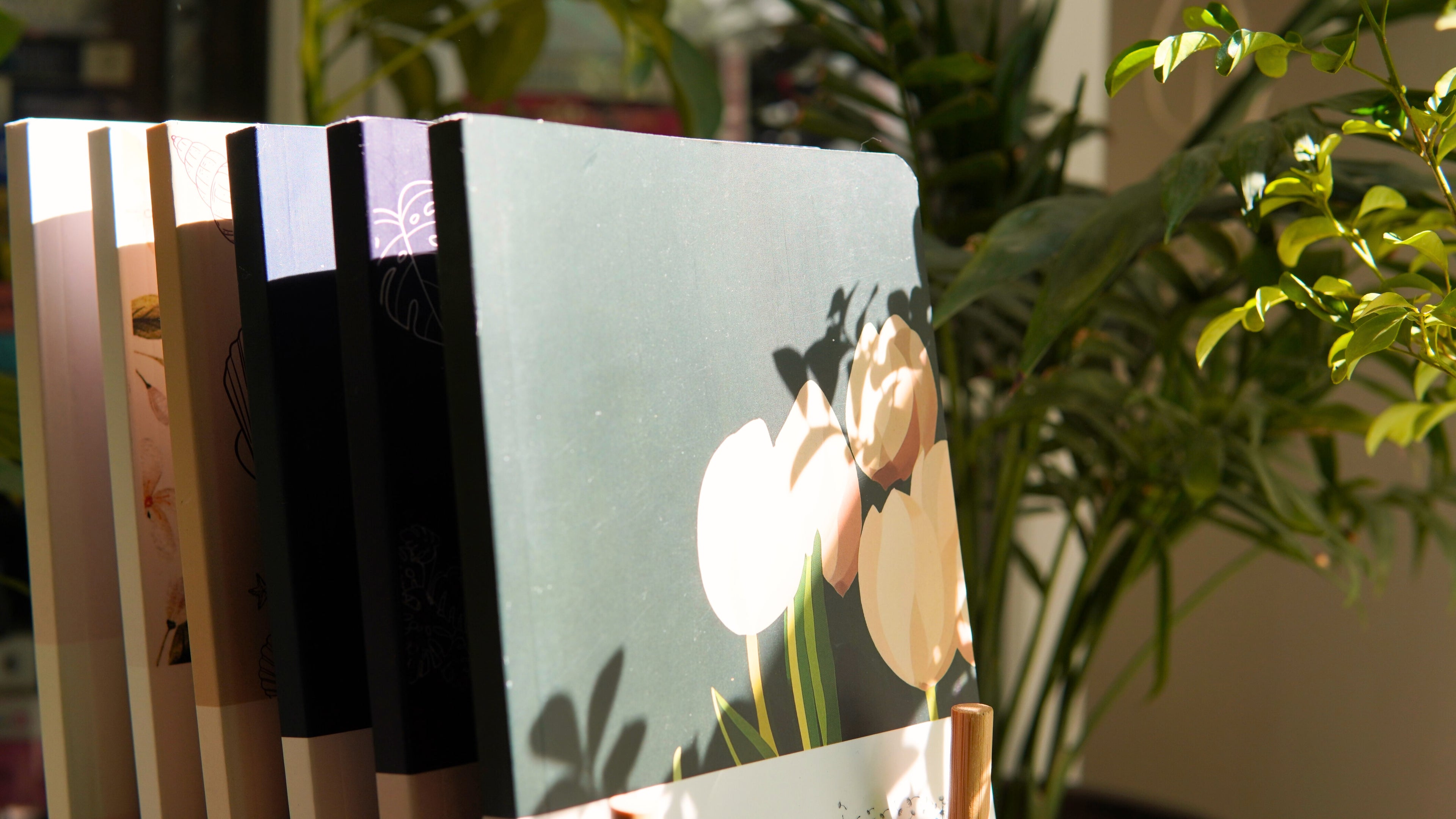 Set of notebooks with floral design on a stand with plants in the background
