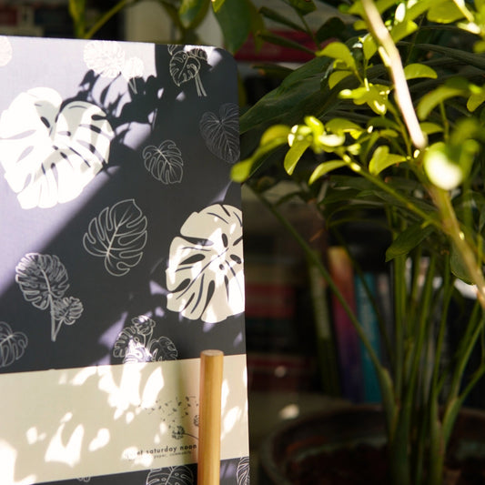 Notebook with monstera leaf pattern on a stand next to a potted plant