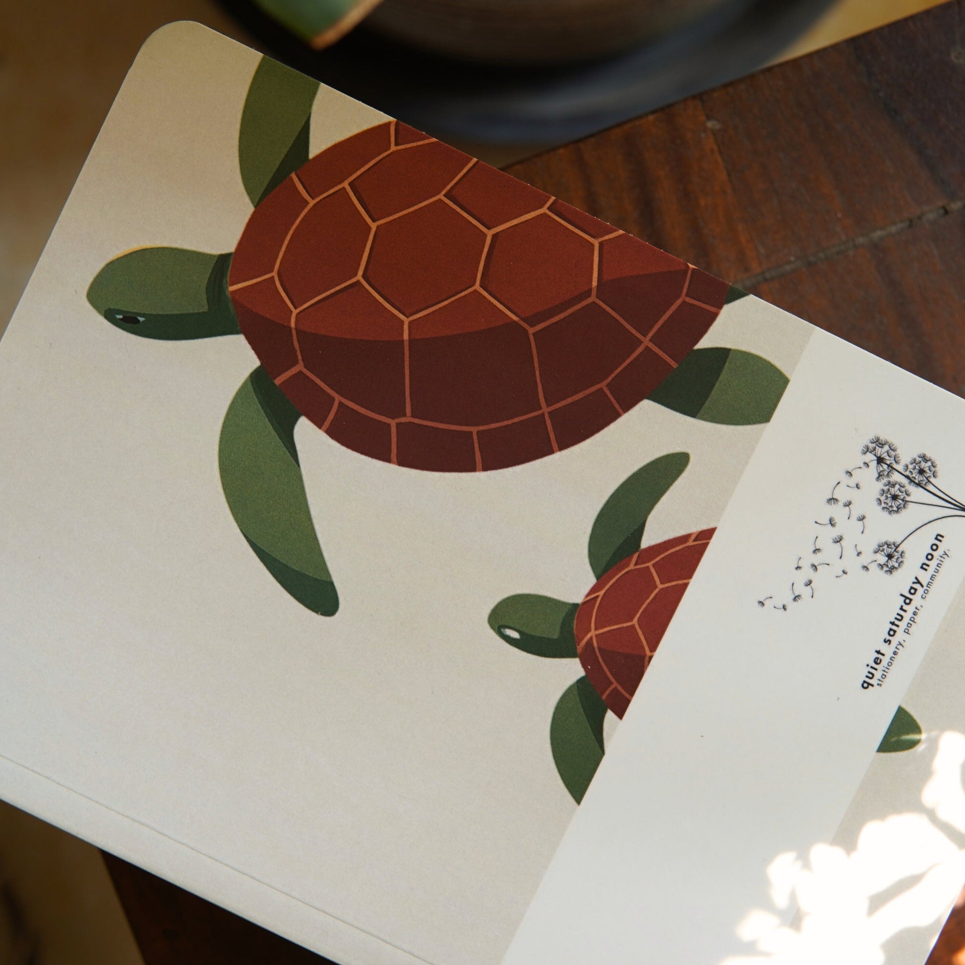 Notebook with turtle design on cover and white card with text on wooden surface